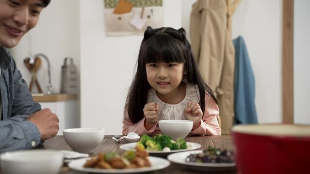 selective focus of hungry Asian girl saying wow with admiration her mom is serving tasty food on dining table. she picks up her chopsticks getting ready to eat