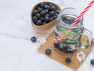 Infused water with fresh organic blueberries and drinking straw on marble background. Space for your text. .