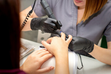 Manicure master in rubber gloves applies an electric nail file to remove the nail polish in a nail salon