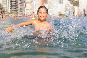 Funny kid spalshing water on an urban beach - obrazy, fototapety, plakaty