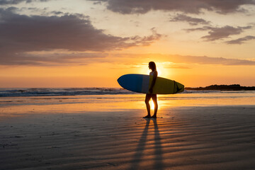 Surfer girl silhouette. Surf woman walking with surfboard on the beach. Golden hour beautiful colors