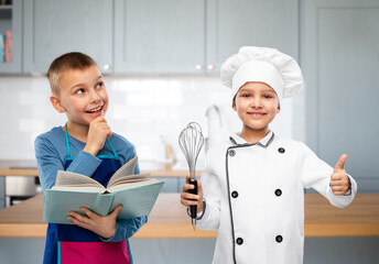 cooking, culinary and profession concept - happy smiling little boy and girl with cook book and whisk over kitchen background
