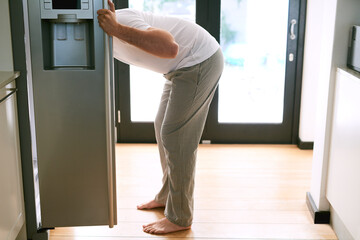 This is how modern man hunts for food. Shot of a man peering into the fridge at home.