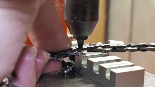 Man removes link pin from a chain saw with special machine. Close-up shot with selective focus