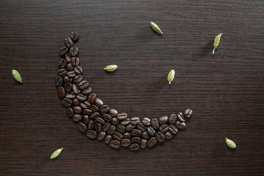Roasted coffee beans arranged in a shape of moon, surrounded by green cardamom pods. Conceptual photo for 24 hour Arabic cafe or Eid and Ramadan celebrations.