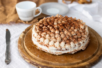 Homemade tiramisu cake with cocoa on top on wooden platter on white tablecloth