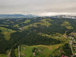 Green slopes of Ukrainian Carpathian mountains in summer. Cloudy morning, low clouds. Aerial drone view.