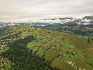 Green slopes of Ukrainian Carpathian mountains in summer. Cloudy morning, low clouds. Aerial drone view.