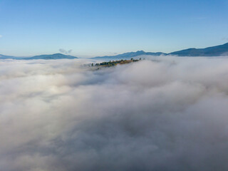 Flight over fog in Ukrainian Carpathians in summer. A thick layer of fog covers the mountains with a solid carpet. Mountains on the horizon. Aerial drone view.