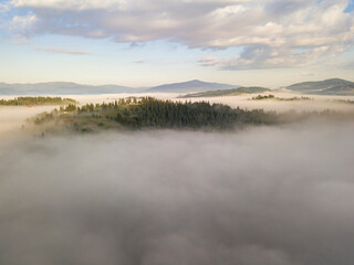Flight over fog in Ukrainian Carpathians in summer. Mountains on the horizon. A thick layer of fog covers the mountains with a continuous carpet. Aerial drone view.