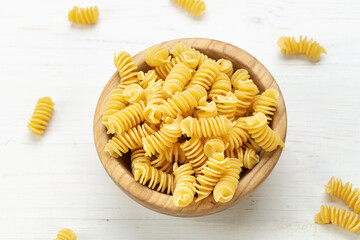 Raw Pasta Fusilli in Wooden Bowl on White Rustic Background.