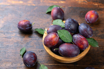 Fresh plums with leaves in a wooden bowl on a brown table.