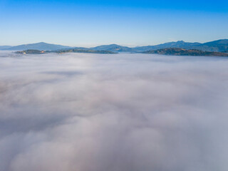 Flight over fog in Ukrainian Carpathians in summer. Mountains on the horizon. A thick layer of fog covers the mountains with a continuous carpet. Aerial drone view.