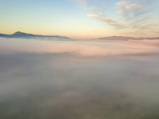 The rays of dawn over the fog in the Ukrainian Carpathians. Aerial drone view.