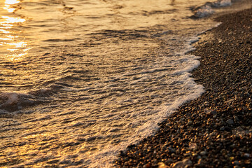 Sea wave on a pebble beach at sunset background