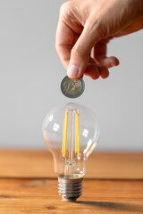 electricity, energy crisis and power consumption concept - close up of hand with coin and lightbulb on wooden table © Syda Productions
