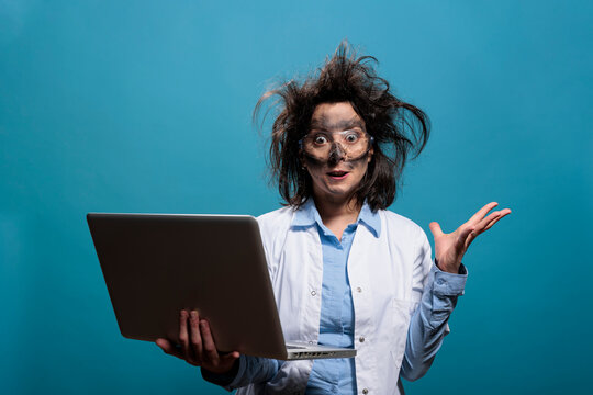 Lunatic chemist with messy hair and dirty face having laptop while gesticulating angrily after dangerous lab explosion. Insane scientist being enraged after failed laboratory chemical experiment.