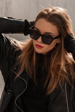 Fashionable beautiful hipster girl with stylish vintage sunglasses in a leather jacket and hoodie in the city. Female fashion style and beauty