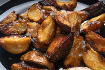 Rustic fried potatoes on a black dish on the table, top view