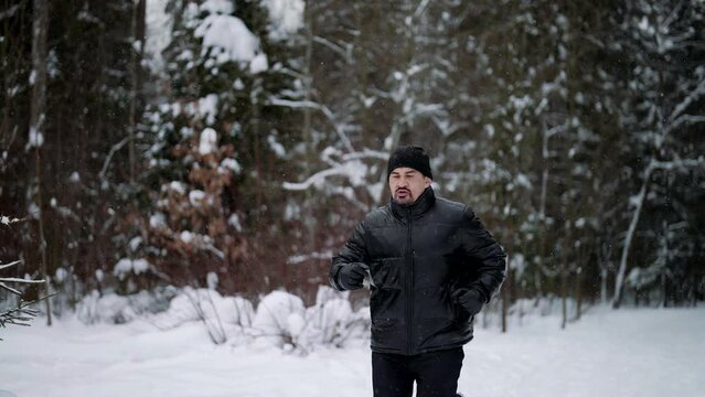 middle-aged man is training in forest in winter day, running over snow and breathing cold air