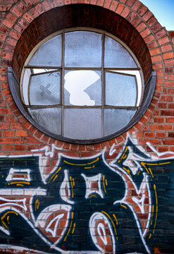 Rundes zerbrochenes altes Fenster in einer Steinmauer mit Graffiti