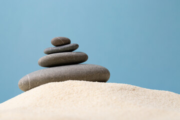 Pyramid of the balanced grey stones on sand besides blue background.