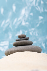 Fototapeta na wymiar Pyramid of the balanced grey stones on sand besides blue background.