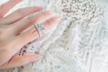 Close up of an elegant diamond ring on woman finger white flower background. love and wedding...