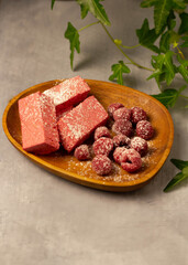Marshmallows with raspberries on a wooden plate. There are green leaves nearby