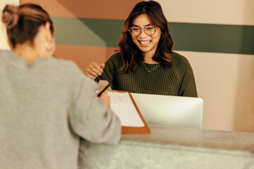 Cheerful receptionist assisting a woman with signing in to an office