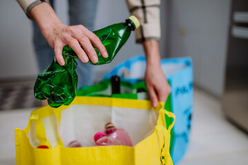 Unrecognizable woman throwing empty plastic bottle in recycling bin in kitchen.