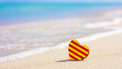 Flag of the Catalonia in the shape of a heart on a sandy beach. The concept of the best vacation in Catalonia resorts