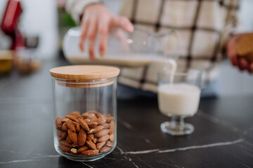Woman pouring almond milk into a glass in kitchen. Healthy vegan product concept.