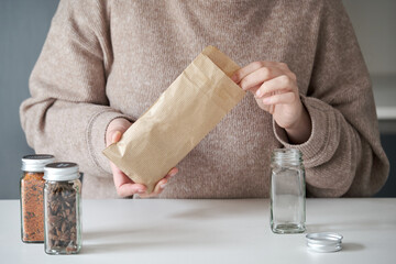 Unrecognizable woman refilling spice jar from a paper bag buyed at package free grocery store.