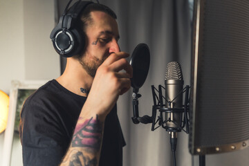 a tattooed good-looking bearded young man with headphones singing in the microphone studio shot...