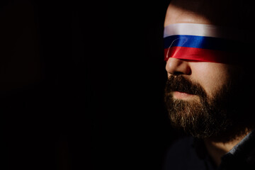 Man with Russian flag blindfold on black background, Russian propaganda closed people's eyes...