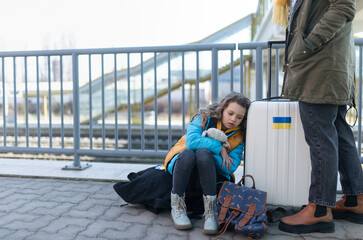 Sad Ukrainian immigrants with luggage waiting at train station, Ukrainian war concept.