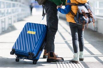 Low section of Ukrainian immigrant family with luggage at train station, Ukrainian war concept.