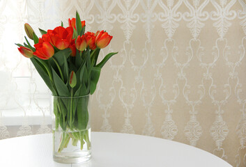 a bouquet of red tulips in a glass vase on a white table.Spring bouquet of flowers in a vase