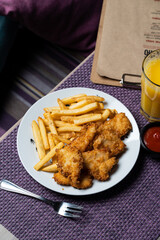 A portion of french fries with deep fried chicken nuggets, top view on dark purple background