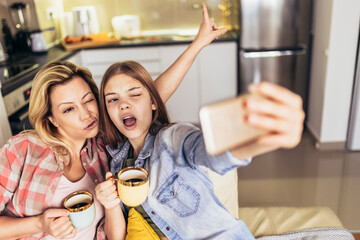 Mother and daughter drink tea or coffee and make selfie with phone.