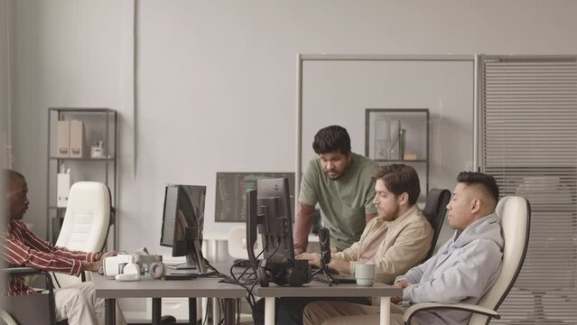 Slowmo of multiethnic team of four video game or software developers working together in modern office equipped with computer monitors. One of men sitting in wheelchair