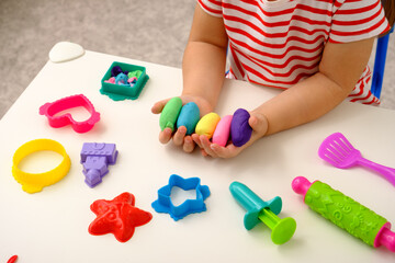 closeup children's hands with multicolored plasticine or playdough on white table with toys,...