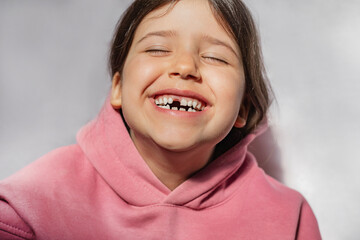 portrait of a beautiful emotional caucasian girl in a pink sweatshirt who lost her first tooth. Close-up of a child with a smile and joy