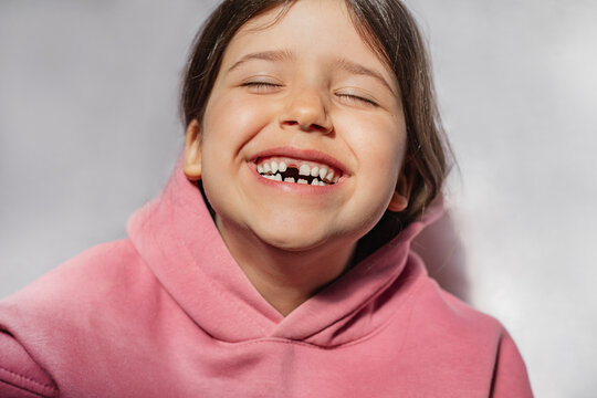 Portrait Of A Beautiful Emotional Caucasian Girl In A Pink Sweatshirt Who Lost Her First Tooth. Close-up Of A Child With A Smile And Joy