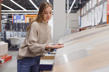 Young woman choosing floor cover, laminate in hardware store