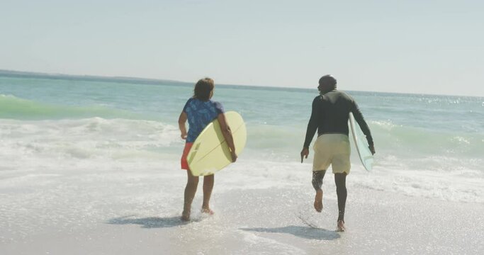 Senior african american couple running with surfboard on sunny beach