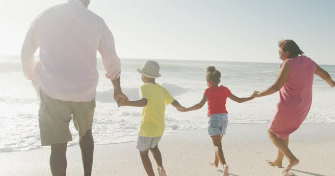 Smiling Senior African American Couple Running With Grandchildren On Sunny Beach