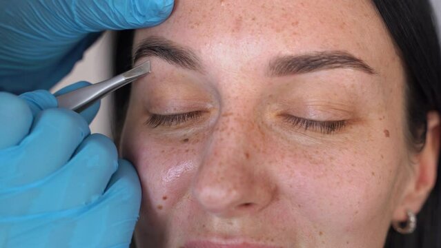 close-up beautiful female eyebrows and gloved hands pluck the hairs under the eyebrow