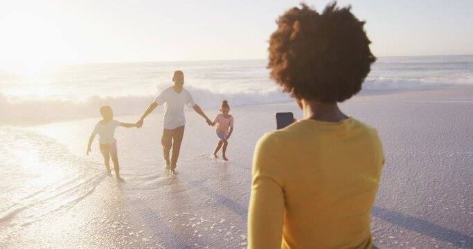 Smiling african american family taking photo and walking on sunny beach